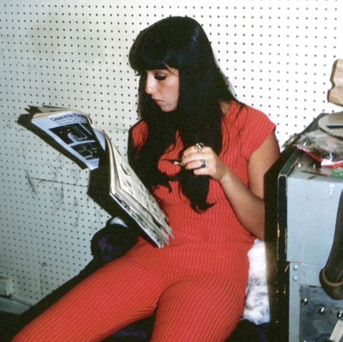 Cher (Taurus), wearing all red, reads a magazine